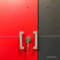 . The image shows a red and dark gray surface with metallic elements. There is a metallic lock with a key inserted into it, and the key has a keychain attached. The lock is mounted on the red part of the surface, and the design includes screws with an industrial look. The website "www.Garten-Q.de" is visible in the bottom right corner.