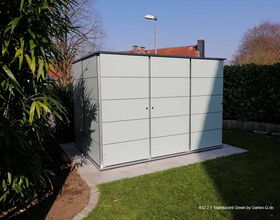 Ein Gartenhaus mit modernen Paneelen, umgeben von Pflanzen und Rasen.