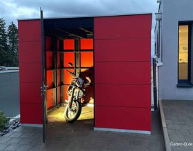 . Rotes Gartenhaus mit offenem Tor, darin ein beleuchtetes Motorrad.