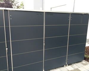 . The image shows a row of gray, rectangular panels that appear to be part of a storage shed or outdoor cabinet. They are metallic with vertical lines dividing each panel. The structure is situated on a paved area.
