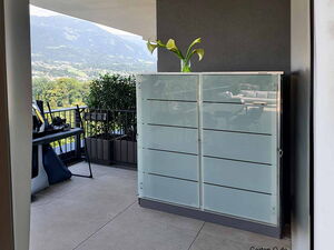 Ein Balkon mit Blick auf die Berge, Pflanze auf Kasten, Gartenmöbel, Geländer und Topfpflanzen.