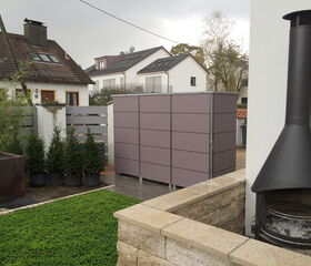 . Ein moderner Garten mit Grill, Lavendel-beige Sichtschutz, Rasen, Pflanzen und Häusern im Hintergrund.