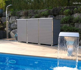 Ein moderner Poolbereich mit Wasserfall, grauem Gartenhaus, Außendusche, Pflanzen und einer Steinmauer im Hintergrund.