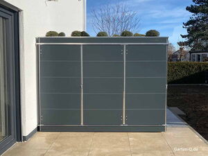 Ein moderner, grauer Gartenschrank mit Pflanzen oben drauf, an einer Außenwand, umgeben von Terrasse und Garten.