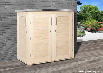 The image shows a wooden outdoor storage unit or cabinet, placed against a gray brick wall. The cabinet has two doors with handle grips and appears to be located on a wooden deck. In the background, there's a garden with green trees, bushes, and flowers.