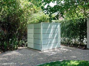 . Ein moderner Gartenschrank aus Metall steht auf einem Kiesplatz, umgeben von Bäumen und Sträuchern im Garten.