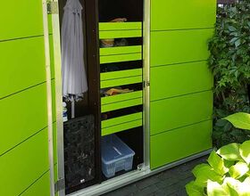 The image shows a green outdoor storage cabinet with open doors, revealing shelves inside. The cabinet contains various items, including a plastic storage box, garden tools, and possibly some clothing hung on the side. The setting appears to be a garden or patio area, with plants visible around the cabinet.