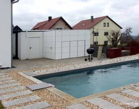 Ein moderner Garten mit Pool, Kieselweg, Grill und weißen Schränken neben einem Haus in einer Wohngegend.