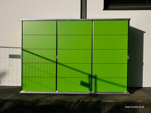 . The image shows a green outdoor storage unit with three doors, likely made of metal. There are shadows cast on it, possibly from a fence, and the website "www.Garten-Q.de" is visible in the bottom right corner.