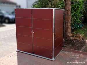 . Ein rotes Gartenschrank aus Metall steht auf einem gepflasterten Weg neben einem Baum und Büschen.