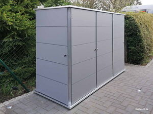 . Ein moderner, grauer Gartenschrank steht auf einem gepflasterten Weg, umgeben von Bäumen und Sträuchern.