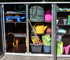 . Ein offener Gartenschrank mit Gartengeräten, Eimern, Gießkannen und verschiedenen Gartenutensilien.