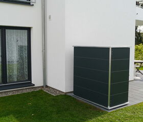 . Ein moderner Außenbereich mit Terrassenplatten, Fenster, grüner Rasen und eine Verkleidung an der Hauswand.