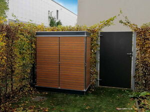 . Ein Gartenhaus mit Holztüren, rechts eine schwarze Tür, umgeben von Hecken.