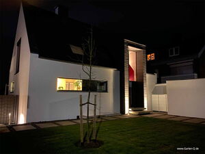 . Ein modernes Haus bei Nacht, beleuchtet mit einem erleuchteten Fenster und einem gepflegten Garten.