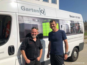 . Zwei Männer vor einem Lieferwagen von Garten[Q] mit Werbung für Gartenschränke, Müllboxen und Unterstände.