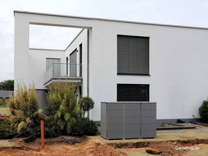 . Modernes weißes Gebäude mit Balkon, Jalousien, Pflanzen und grauem Schrank im Vorgarten.