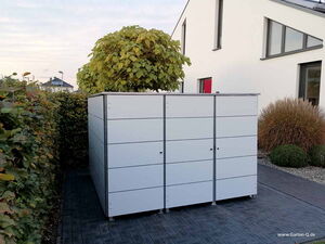 . Ein moderner weißer Gartenschrank steht auf einem gepflasterten Weg, umgeben von Hecken und einem modernen Haus.