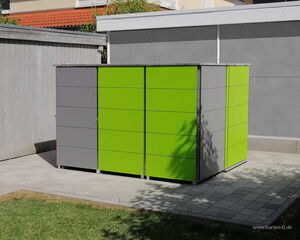 . The image shows a modern storage unit or shed, with green and gray panels. It is placed on a tiled patio with a bit of grass visible. The unit is set against a fence and next to a larger structure.