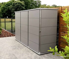 . Moderner, grauer Gartenschrank neben Holzzaun, umgeben von Pflanzen und einem Zaun.