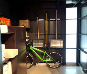 . Fahrrad, Regale mit Kartons, Werkzeuge an der Wand, helle Industrielampe.