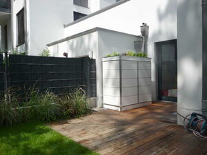 . Ein moderner Garten mit Holzterrasse, Pflanzen, Metallzaun, Aufbewahrungsbox und Schlauchrolle.