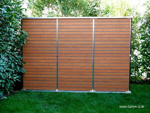 . The image shows a wooden garden shed or storage unit with horizontal slats. It's surrounded by greenery, including bushes and grass. The structure appears to be made of wood with metal or similar vertical supports.