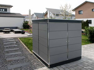 . Ein moderner Gartenschrank steht in einem gepflegten Garten mit Terrasse und Lounge-Möbeln im Hintergrund.