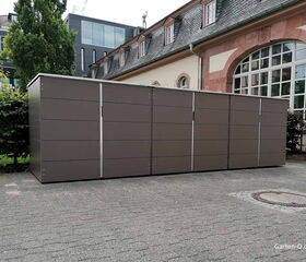 . Ein großer, moderner Schuppen im Freien, neben einem Gebäude, umgeben von Bäumen und einem Zaun.
