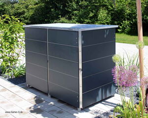 . The image depicts a metal storage unit situated outdoors, likely designed for garden use. It is rectangular and appears to have a hinged door or doors. Surrounding it are various plants and flowers, set on a stone or tiled surface, with greenery visible in the background.