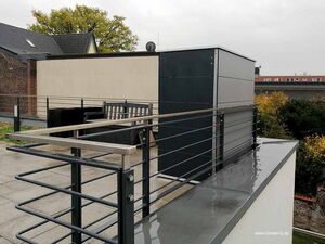 . Eine Dachterrasse mit modernen Metallgeländern und einem Sitzbereich, umgeben von Bäumen und Gebäuden.