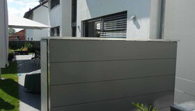 . Moderne Hausfassade, Terrasse mit Sonnenschirm, mehrere Pflanzen, HPL-Trespa-Verkleidung.