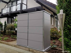 . Ein modernes Gartenhaus neben einem zeitgenössischen Gebäude mit Pflanzen und einem Metallfackelständer.