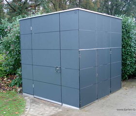 Ein modernes, quadratisches Gartenhaus in einer Hofecke mit grauen Paneelen umgeben von Pflanzen.
