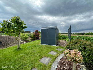 . Ein moderner Gartenschuppen auf einem gepflegten Rasen mit Bäumen und Büschen unter bewölktem Himmel.