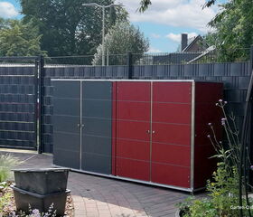 . Gartenschrank vor einem Zaun in einem Garten, umgeben von Pflanzen und Büschen.