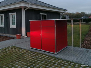 . Ein modernes rotes Gartenhaus neben einem grau gestrichenen Haus mit zwei Fenstern und zwei Töpfen.