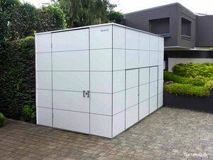 . Ein moderner, quadratischer Gartenschuppen aus Metallpaneelen neben einem Haus und Garten.