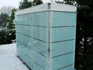 . Ein moderner Gartenschrank aus Glas und Metall steht im schneebedeckten Garten.
