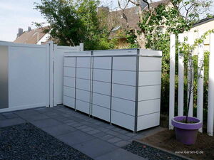 . The image depicts an outdoor setting with a modern storage unit, possibly for a garden or patio area. The unit is rectangular with a sleek design, made of white panels with metal frames. It is placed on a paved area with a gravel border. There is a white fence to the left and a white post fence to the right. A tree and other greenery are visible in the background, and there is a purple planter with a small tree next to the storage unit.