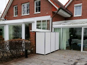 . Backsteinhaus mit verglaster Terrasse, Hecke und Holzboden, modern gestaltet.