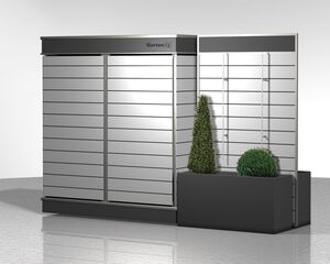 The image shows a modern outdoor storage unit with a sleek, horizontal slat design. It includes a planter section with two small ornamental bushes, one conical and the other spherical. The unit appears to be modular and is labeled with "Garten[Q]" on the top. The overall color scheme is metallic and neutral.