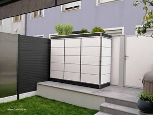 . The image shows a modern storage unit placed outdoors on a concrete platform. The unit has a sleek design with horizontal lines. There are some decorative plants on top of it. It's situated in a backyard or garden area with a well-maintained lawn, surrounded by privacy fences on two sides. There's a set of steps leading up to the platform, and a potted plant is visible next to the storage unit.