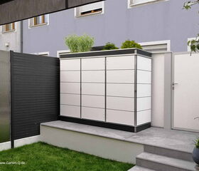 . Ein weißer Gartenschrank auf einer Terrasse neben einem grauen Zaun und einer Topfpflanze.