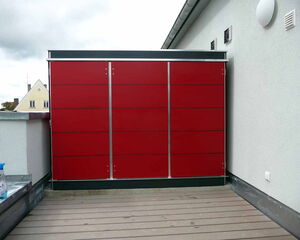 . Rot verkleideter Außenschrank auf einer Dachterrasse, daneben ein Sprühreiniger auf der Mauer.