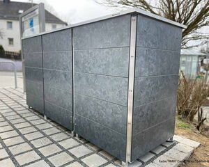 Ein grauer Metallschrank steht auf gepflastertem Boden im Freien.