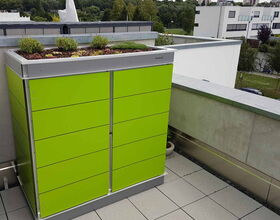 . Ein grüner Schrank mit bepflanztem Dach auf einer Terrassenfläche, umgeben von moderner Architektur.