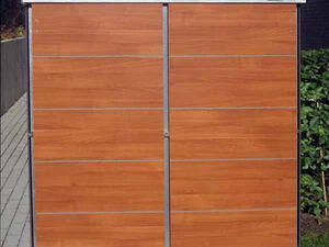 . The image shows a wooden garden shed or storage unit with a sleek, modern design. It appears to have horizontal panels and is situated on a tiled pathway, with some vegetation around it.