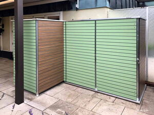 . Ein moderner, grüner Gartenschrank mit Holzoptik in einem gepflasterten Außenbereich.