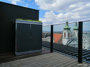 . Ein Dachgarten mit einem Schrank und Blick auf kirchliche Gebäude und blauen Himmel.